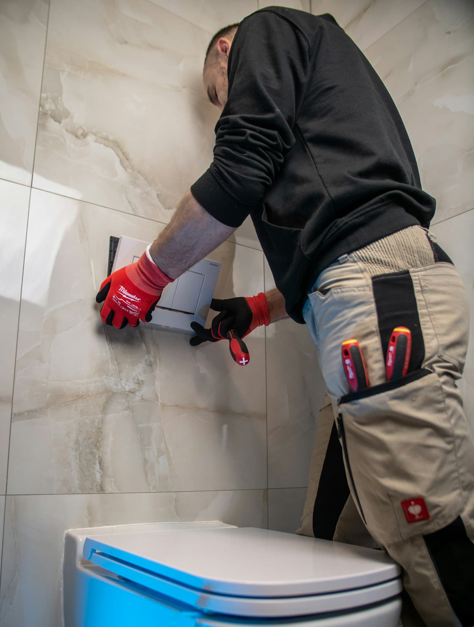 Plumber repairing a wall-mounted toilet cistern in a tiled bathroom